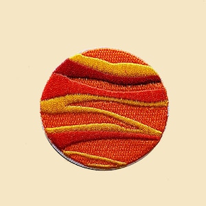 Könnte beinhalten: Ein runder, orangefarbener und gelber gestickter Aufnäher mit einem wellenförmigen Muster. Der Aufnäher ist perfekt, um Kleidung, Taschen oder anderen Accessoires einen Hauch von Farbe und Persönlichkeit zu verleihen.