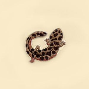 May include: A brown and black embroidered patch of a salamander with a red underbelly.