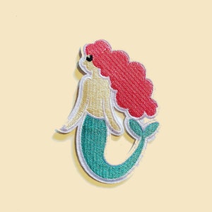 May include: An embroidered iron-on patch featuring a cartoon mermaid with red hair, a yellow bodice, and a teal tail.