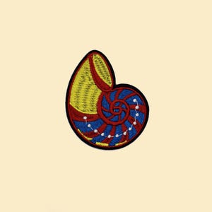 May include: Embroidered patch with a seashell design in yellow, red, and blue, outlined in black. The spiral design includes white dots. The patch is suitable for clothing or accessories.
