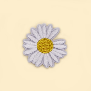 Puede incluir: Parche bordado de margarita con pétalos blancos y centro amarillo. El parche tiene un borde gris claro y está sobre un fondo amarillo pálido. Este parche floral es adecuado para ropa y accesorios.