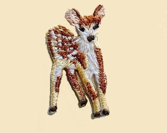 May include: Embroidered iron-on patch of a brown and white fawn with white spots. The fawn is standing on all four legs with its head turned to the side.