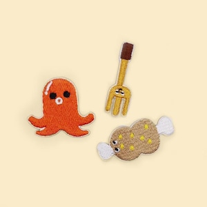 May include: Three embroidered patches: an orange octopus, a yellow fork, and a brown food item with white accents. The patches are on a light yellow background.