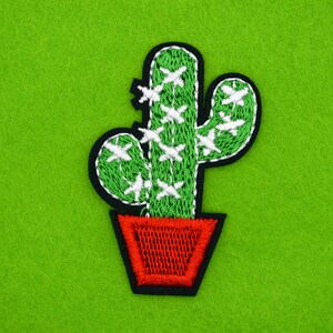 May include: Green embroidered cactus with white stitching, in a red pot, on a green felt background.