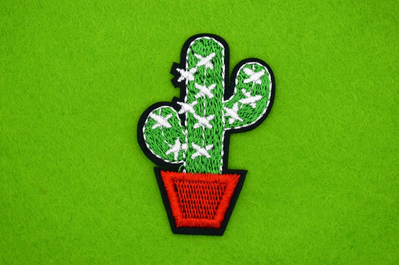 May include: Green embroidered cactus with white stitching, in a red pot, on a green felt background.