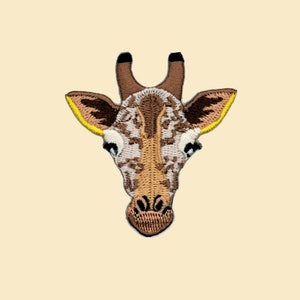 Könnte beinhalten: Gestickter Aufnäher mit dem Gesicht einer Giraffe mit braunem und weißem Fell, schwarzen Augen und einem gelben Ohr.