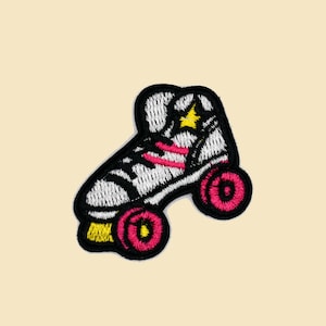 Op de afbeelding: Een geborduurde patch van een witte en zwarte rolstoel met roze wielen en een gele ster aan de zijkant.