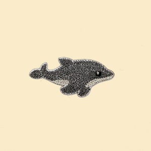 May include: A gray embroidered dolphin patch with a white belly, perfect for adding a playful touch to clothing or crafts.