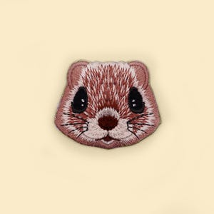 May include: Embroidered patch of a brown and pink squirrel face with black eyes.