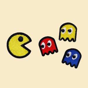 Può includere: Personaggio giallo Pac-Man con la bocca aperta, che insegue tre fantasmi. Un fantasma è rosso, uno è blu e uno è giallo.