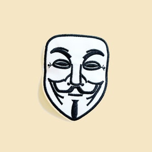 May include: White embroidered patch depicting the Guy Fawkes mask, with black detailing and a black border. The patch is set against a pale yellow backdrop. The design features a distinctive mustache and a smiling mouth.