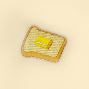 May include: A yellow embroidered patch of a slice of toast with a pat of butter on top.