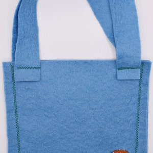 Op de afbeelding: Een lichtblauwe felt tote bag met groene stiksels en een geborduurde bruine kiwi-vogel aan de voorkant.
