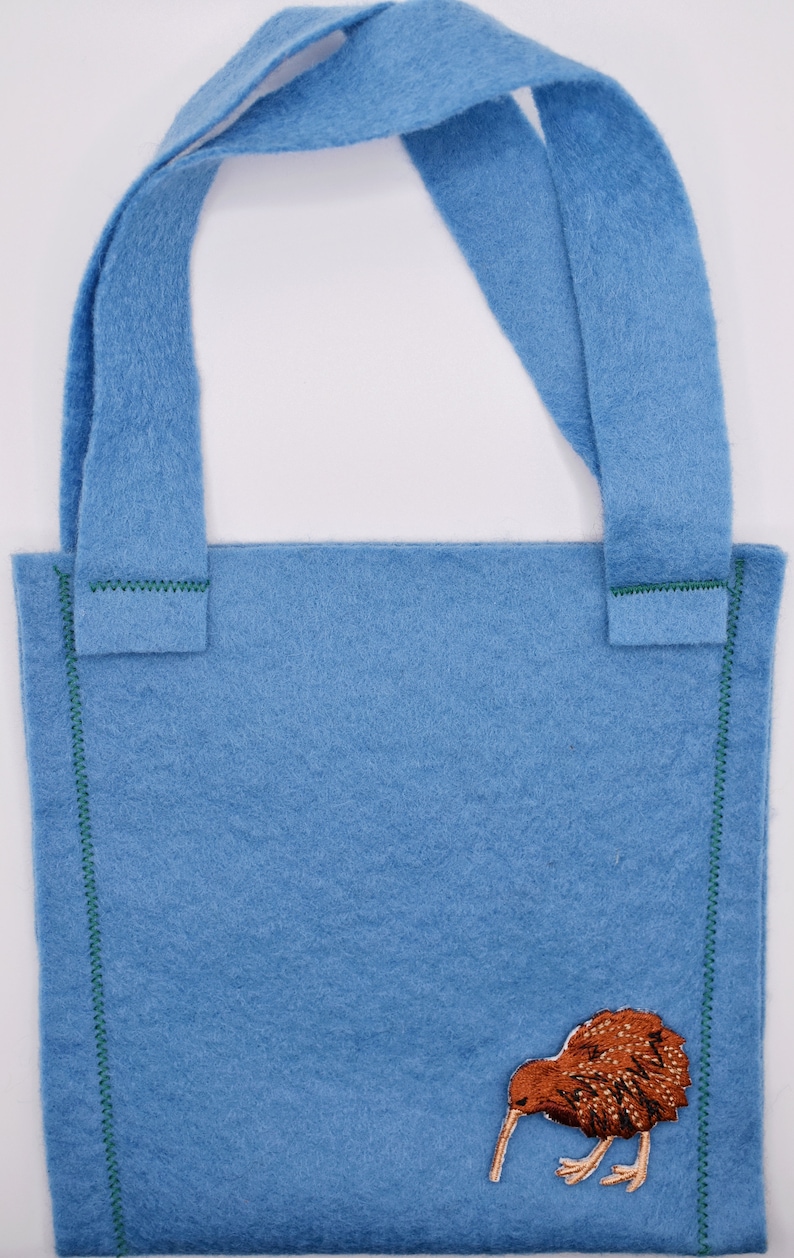 Op de afbeelding: Een lichtblauwe felt tote bag met groene stiksels en een geborduurde bruine kiwi-vogel aan de voorkant.