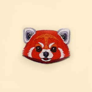 Könnte beinhalten: Gestickter roter Panda-Gesichts-Patch mit weißen Akzenten. Der Patch hat rotes Fell, eine weiße Schnauze und schwarze Augen.