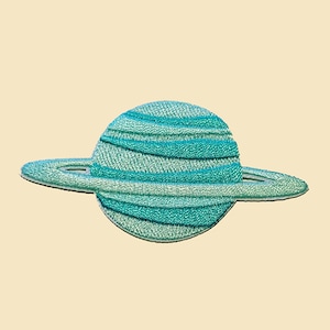 May include: An embroidered patch of the planet Saturn, featuring a teal blue colour and a ring system.