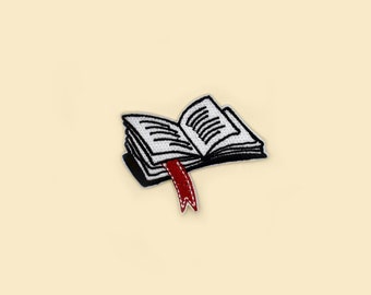 Peut inclure: Un patch brodé en noir et blanc représentant un livre ouvert avec un marque-page rouge. Le livre est ouvert sur une page avec des lignes de texte.