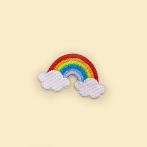 May include: Embroidered rainbow patch with red, orange, yellow, green, blue, and purple arches. Two white fluffy clouds are at the base of the rainbow. The patch is on a light cream background.
