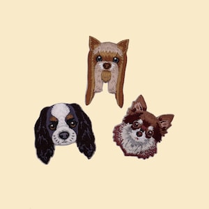 Puede incluir: Tres parches bordados de perros: un Cavalier King Charles Spaniel, un Yorkshire Terrier y un Chihuahua. Los parches presentan costuras detalladas y representaciones realistas de las razas de perros, sobre un fondo crema.