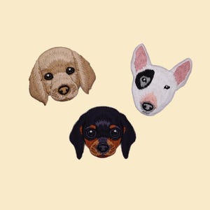 May include: Embroidered patches of three dog faces: a tan poodle, a white Bull Terrier with a black eye patch, and a black and brown Dachshund. Set against a light beige background.