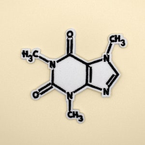 May include: An embroidered patch showing the molecular structure of caffeine in white and black. The patch is a detailed representation of the chemical compound, with a beige background.