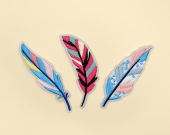 Könnte beinhalten: Drei bunte gestickte Stoff-Patches in Form von Federn. Die Federn sind in Blautönen, Rosa und Gelb.