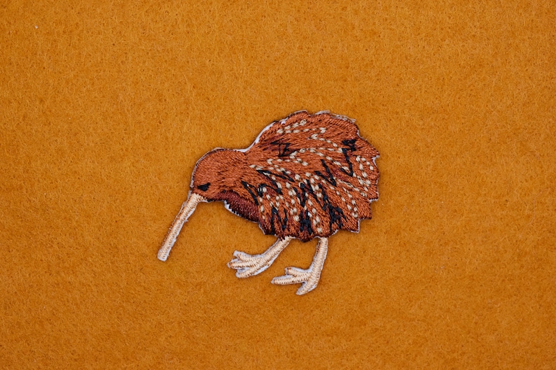 Op de afbeelding: Geborduurde bruine kiwi-vogelpatch met witte accenten op een bruine vilt achtergrond.