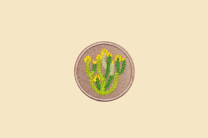 May include: A round, beige fabric patch with an embroidered design of a green and yellow cactus plant.