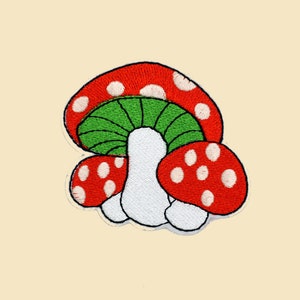 May include: An embroidered patch featuring three red and white mushrooms with green tops. The mushrooms are arranged in a cluster, with the largest mushroom in the center and the two smaller mushrooms on either side.