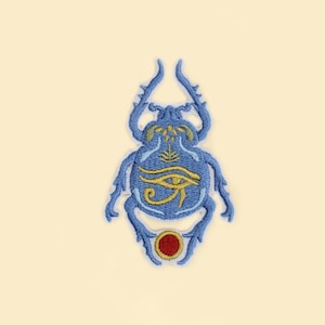 May include: Embroidered patch featuring a blue scarab beetle design with gold accents and an Eye of Horus symbol. The patch has a red circle at the bottom and is set against a cream background. This patch is suitable for clothing or accessories.