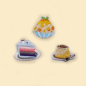May include: Embroidered patches featuring desserts: a layered cake slice, a sundae in a blue bowl, and a custard dessert with a spoon. The patches have detailed stitching and vibrant colors, perfect for decorating clothing or accessories.