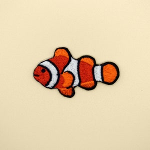 May include: An orange and white embroidered clownfish patch. The fish is swimming to the right.