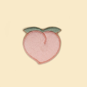 May include: A pink peach embroidered patch with green leaves. The patch is made of soft, fuzzy fabric.