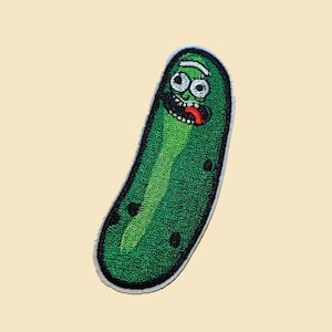May include: An embroidered patch of a green pickle with a face, wearing a white headband and a red tongue sticking out.
