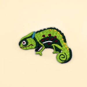 May include: Green embroidered chameleon patch with brown, white, and yellow details. The chameleon is facing left and has a curled tail.