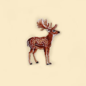 May include: Embroidered patch of a brown deer with white spots and large antlers. The deer is standing on a light yellow background.