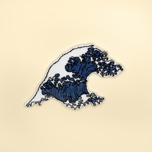 Könnte beinhalten: Ein weißer und blauer gestickter Aufnäher, der eine große Welle darstellt, die an die Große Welle vor Kanagawa erinnert, einen berühmten japanischen Holzschnitt.