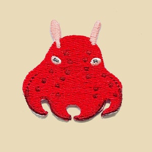 May include: Red embroidered patch of a cartoon octopus with pink ears and white eyes.