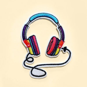 May include: Embroidered patch featuring a colorful headphone design. The headphones have a blue headband, with red, purple, yellow, and pink earcups. A black cord extends from the headphones. The patch is outlined in white.