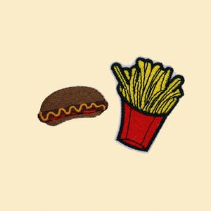 May include: Embroidered patches of fast food items. One patch features a brown hot dog with yellow and red accents. The other patch shows a red container of yellow french fries with black outlines.