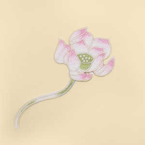 May include: A pink and white embroidered lotus flower with a green center and a long stem. The flower is on a light yellow background.