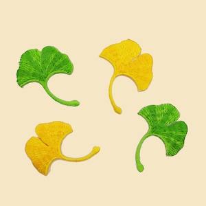 May include: Four embroidered ginkgo leaves, two yellow and two green, arranged in a circular pattern on a light beige background.