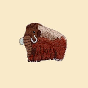 May include: Embroidered patch of a cartoon mammoth. The patch has a brown body with a lighter brown and white back. It has a white tusk and a white curved trunk. The patch is set against a light beige background.