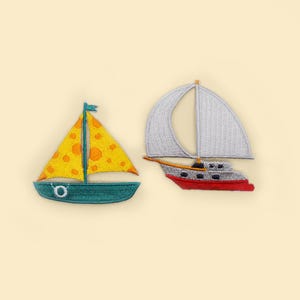 May include: Two embroidered iron-on patches of sailboats. One sailboat is yellow with orange polka dots and a teal hull. The other sailboat is white with a red hull.