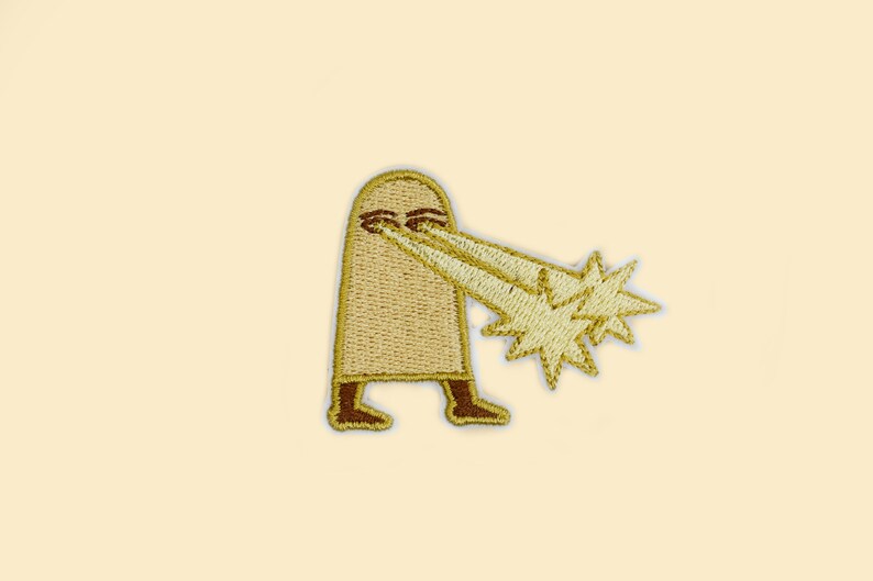 May include: Embroidered patch featuring a cartoon figure with a beige body and brown feet. The figure is shooting golden starbursts from its eyes. The patch has a beige background.