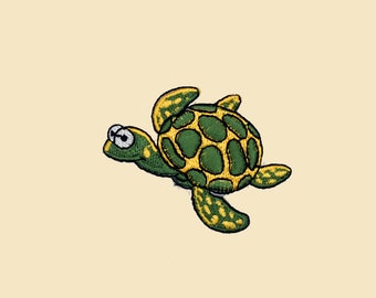 May include: A green and yellow embroidered sea turtle patch. The turtle has a cartoon-like appearance with large eyes and a wide smile.