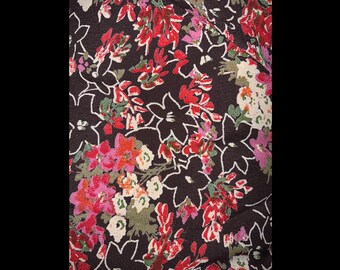 May include: Close-up of a fabric with a floral pattern. The design features red, pink, and white flowers with green leaves on a dark brown background. White outlines define the floral shapes.