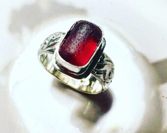 May include: A silver ring with an ornate design and a red glass stone set in the center.
