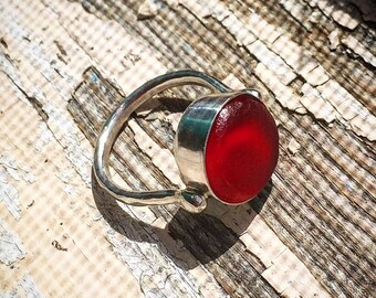 May include: A silver ring with a red glass cabochon. The ring is set on a weathered wooden surface.