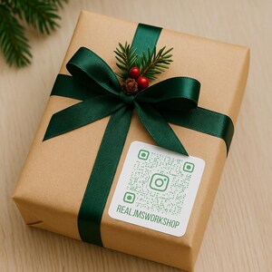 May include: A rectangular gift box wrapped in brown kraft paper, tied with a dark green satin ribbon. The top is decorated with a small sprig of pine needles, two red berries, and a pinecone. A white square sticker features a green QR code.